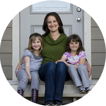 Mother and two daughters, smiling, sitting on front porch of their home