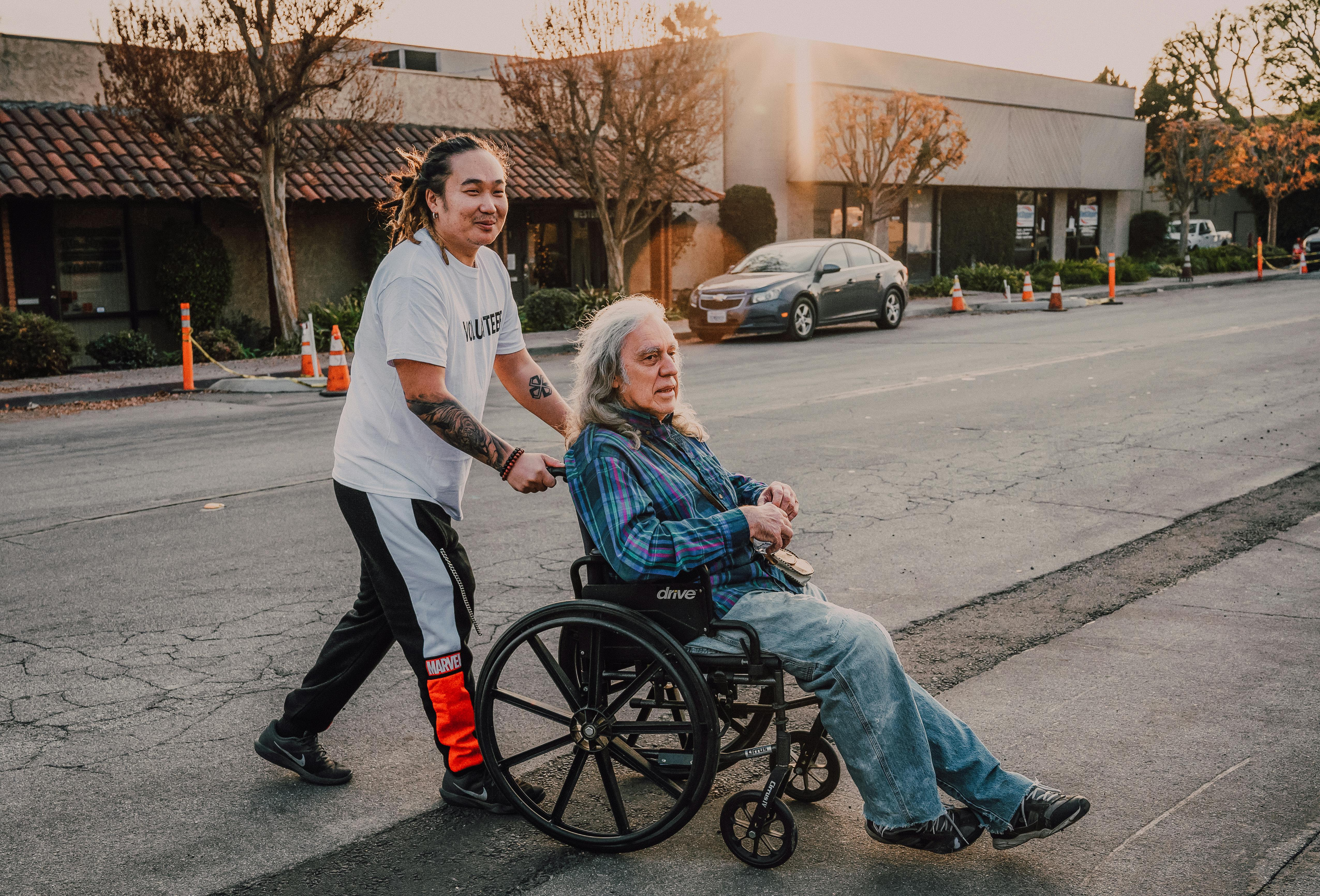 Young man pushing an elderly man in a wheelchair on the street
