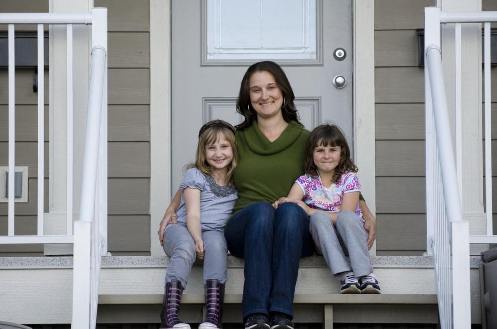 Mother and daughters smiling, sitting on front porch of their home