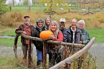Group of people standing by a rustic wooden fence holding a large pumpkin in a community garden