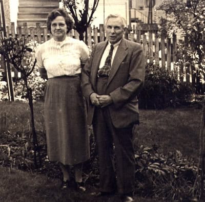 Black and white photo of a couple standing together in a Salsbury Garden, with a wooden fence and houses in the background