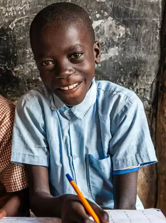 Smiling student holding a pencil and writing in a notebook in a classroom