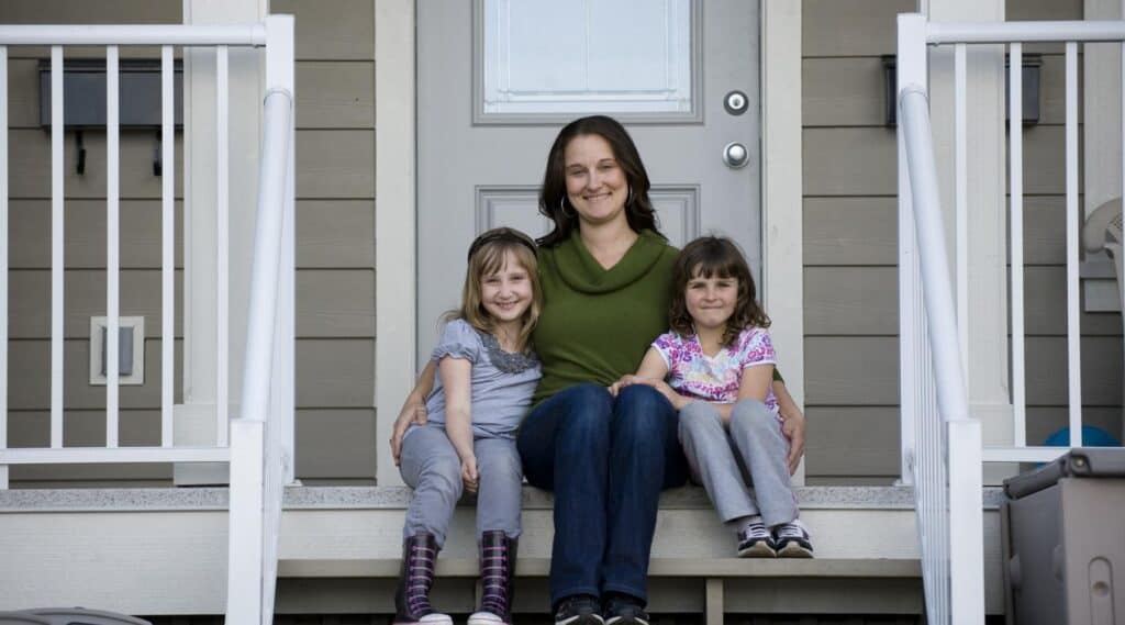 Mother sitting on the front steps of a home with her two young daughters
