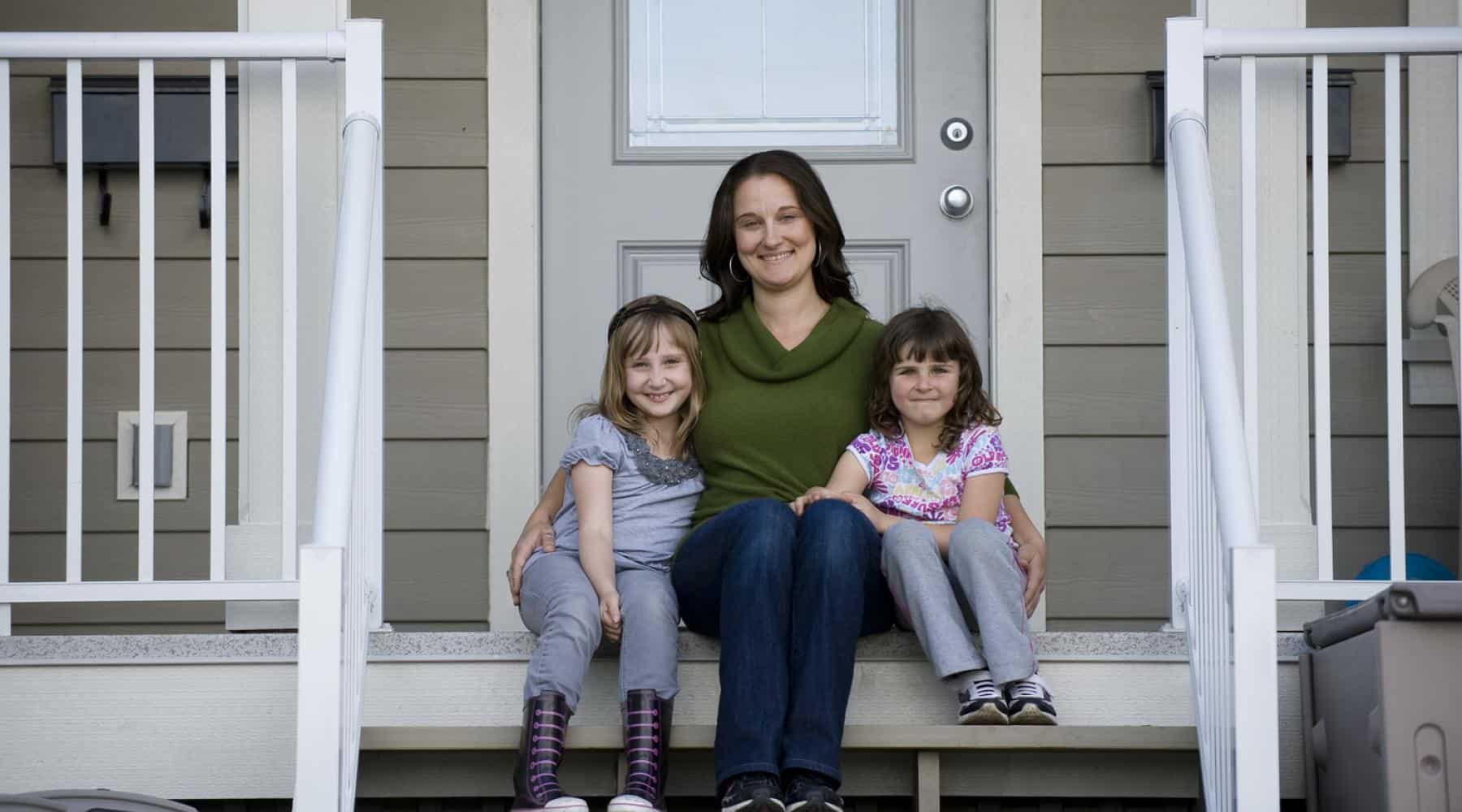 Mother sitting on the front steps of a home with her two young daughters