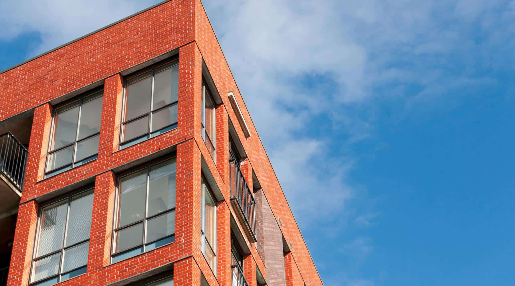 Corner view of a modern red brick apartment building against a blue sky