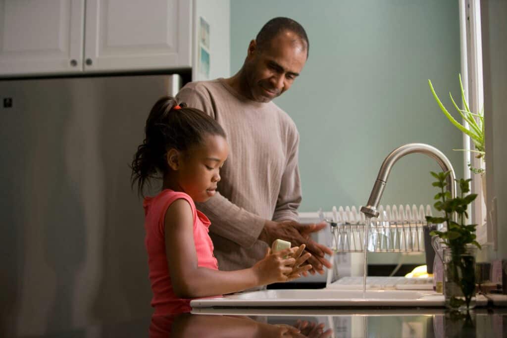 Father and daughter washing hands together at a kitchen sink