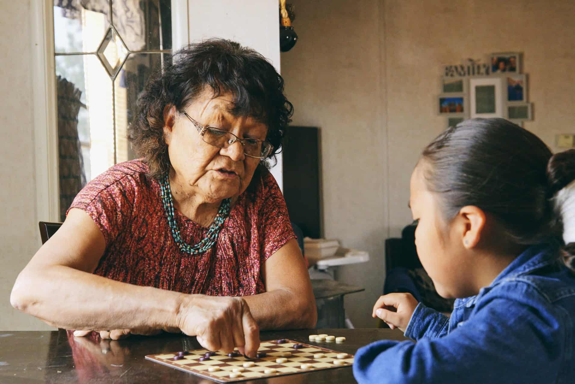 Senior woman teaching a child to play checkers at a table
