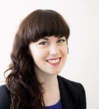 Professional headshot of a smiling woman with long dark hair wearing a black blazer.