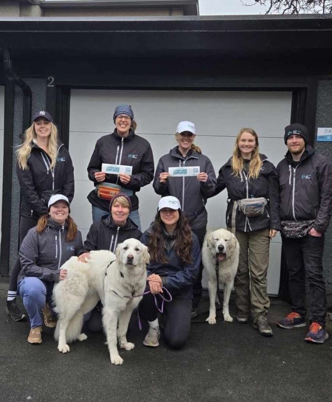 Group of team members with two dogs holding “Living Wage Employer” signs outside a building.