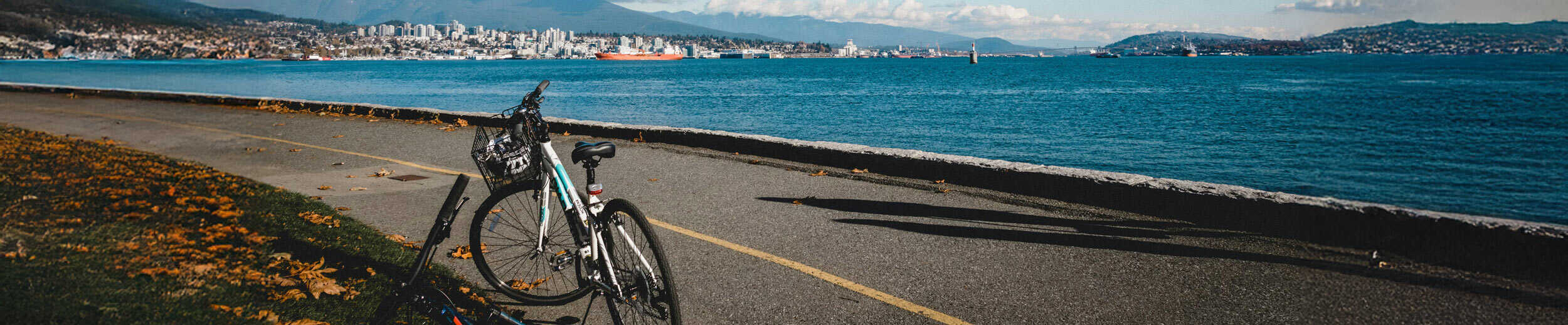 Bicycle parked along Vancouver’s waterfront seawall with downtown skyline and mountains across Burrard Inlet on a sunny day