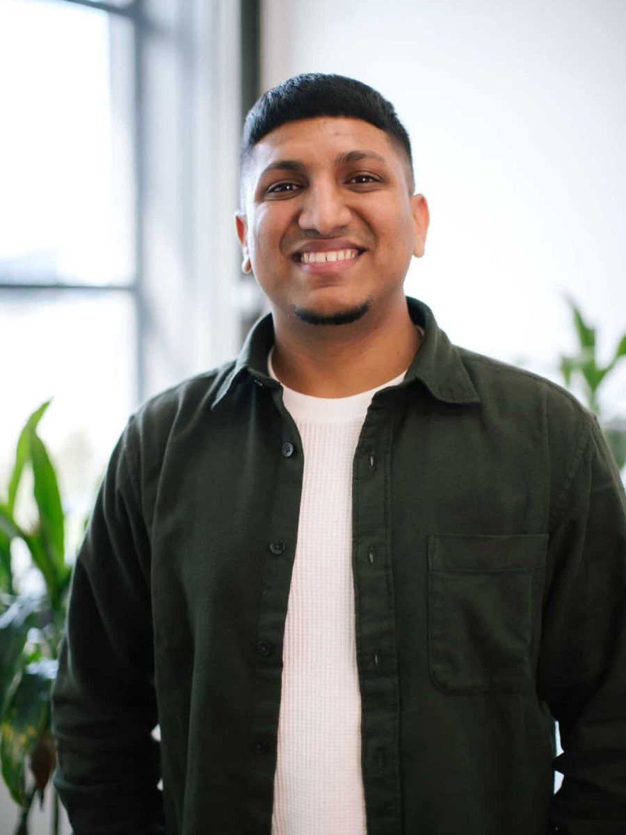 Smiling man wearing a dark green shirt and white T-shirt standing in a bright office